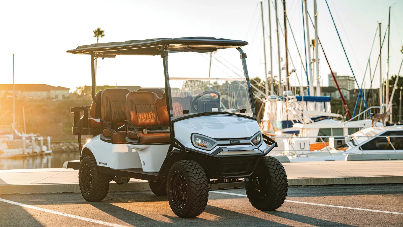 White lifted golf cart parked at a marina at sunset