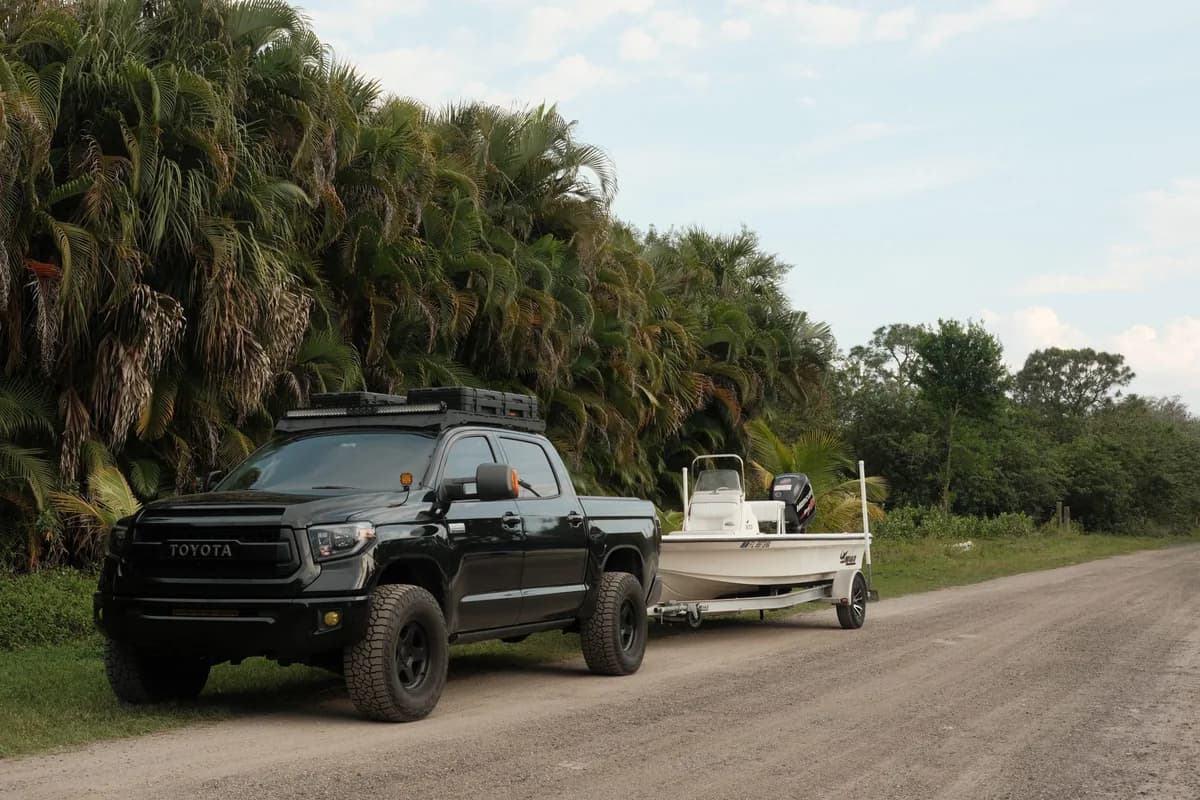 Pickup towing a flats skiff with an outboard down a shell road