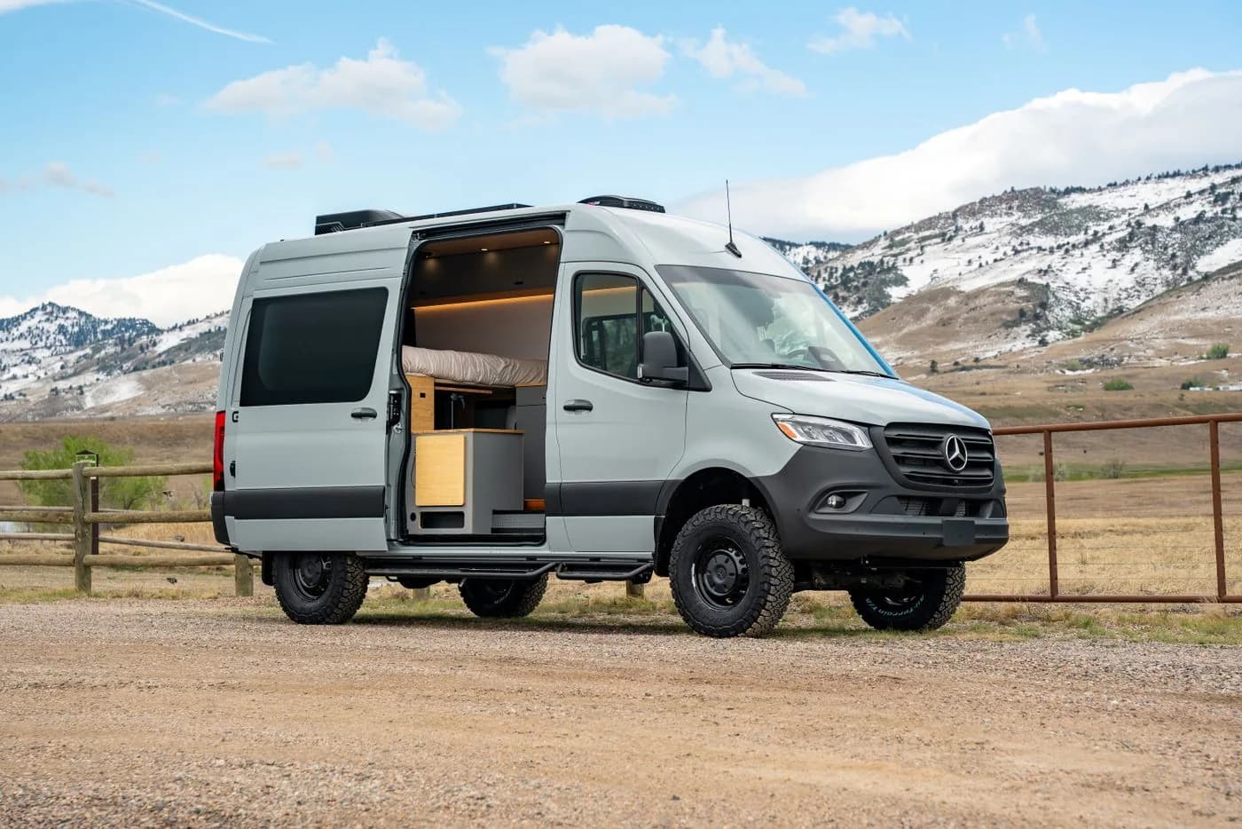 Camper van with its side door open on a gravel pull-off below snowy hills