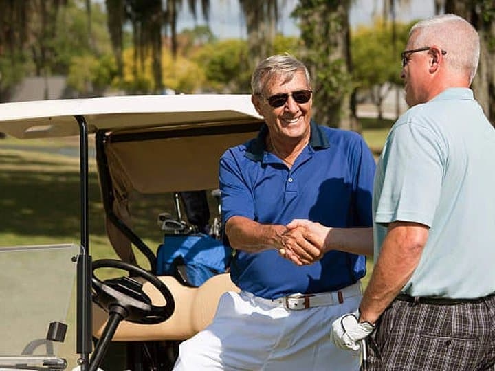 Two golfers shaking hands beside a cart